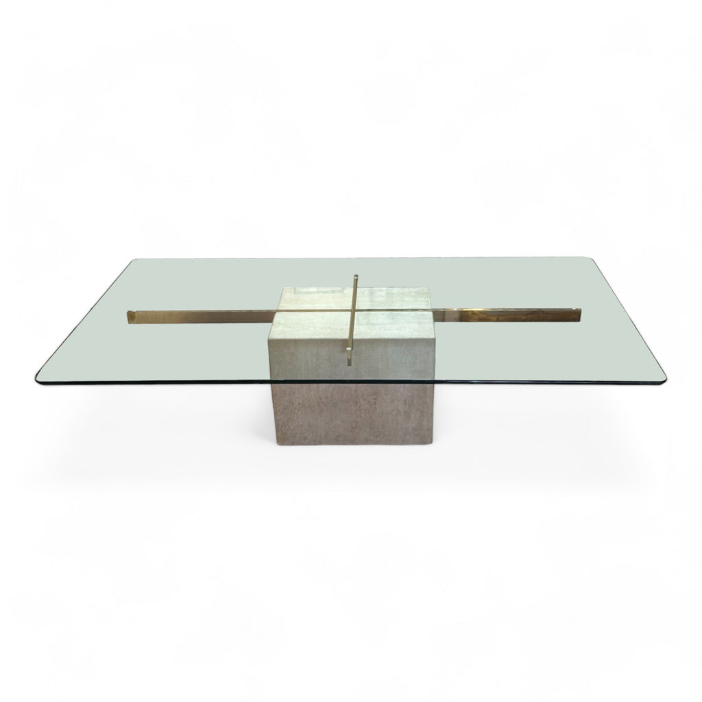 A coffee table with a travertine cube base, brass cross design, topped with a rectangular glass surface. 