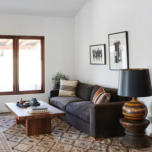 Sofa in livingroom with vintage midcentury ceramic lamp, framed art on wall and wood plank coffee table.