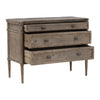 This dresser has a rectangular shape with three wide drawers and a weathered, rustic wood texture. The edges are softly rounded, and the small oval knobs have a smooth finish. Its slim, tapered legs feature subtle carved detailing, adding a refined touch. The overall look is simple yet elegant, with a pale, vintage-style finish.