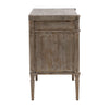 This dresser has a rectangular shape with three wide drawers and a weathered, rustic wood texture. The edges are softly rounded, and the small oval knobs have a smooth finish. Its slim, tapered legs feature subtle carved detailing, adding a refined touch. The overall look is simple yet elegant, with a pale, vintage-style finish.