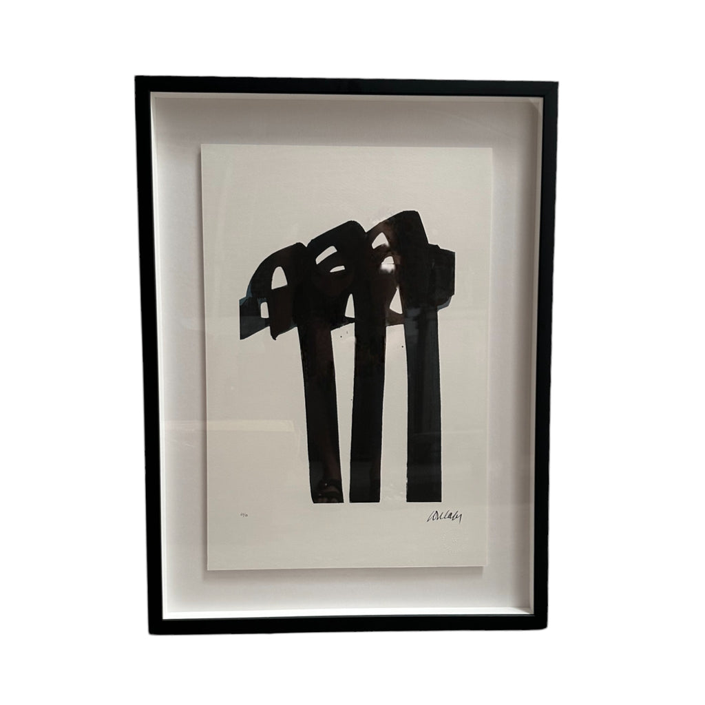 The artwork features bold, thick black brushstrokes that dominate the center of the piece. The strokes are broad, vertical, and slightly curved at the top, giving the impression of abstract columns or arches. The design is minimalist yet dynamic, typical of Pierre Soulages' style, with a stark contrast between the black shapes and the white background. The piece is framed in a sleek, black frame, enhancing its contemporary feel.