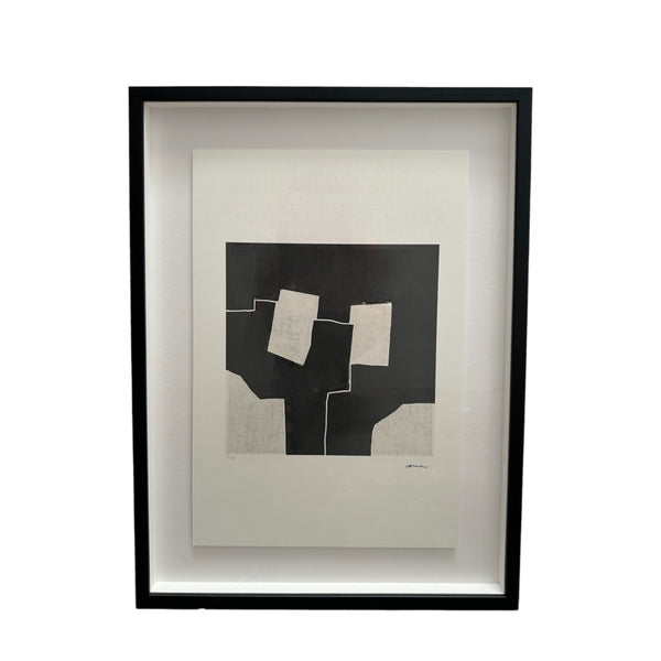 This piece is an abstract artwork by Eduardo Chillida, consisting of large black and white geometric shapes. The central area of the print features several irregular white rectangles arranged on a solid black background, giving the impression of overlapping forms. The design is minimalist, with sharp edges and contrasting tones that create a bold visual effect. It’s framed in a sleek black frame, adding a modern touch to the presentation.