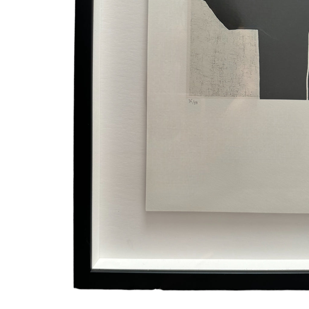 This piece is an abstract artwork by Eduardo Chillida, consisting of large black and white geometric shapes. The central area of the print features several irregular white rectangles arranged on a solid black background, giving the impression of overlapping forms. The design is minimalist, with sharp edges and contrasting tones that create a bold visual effect. It’s framed in a sleek black frame, adding a modern touch to the presentation.