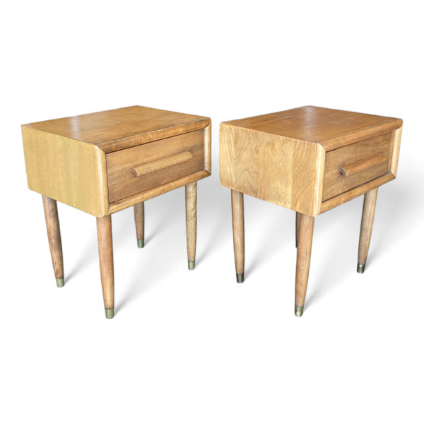 A pair of midcentury modern nightstands with single drawers and tapered legs with a light oak finish. 