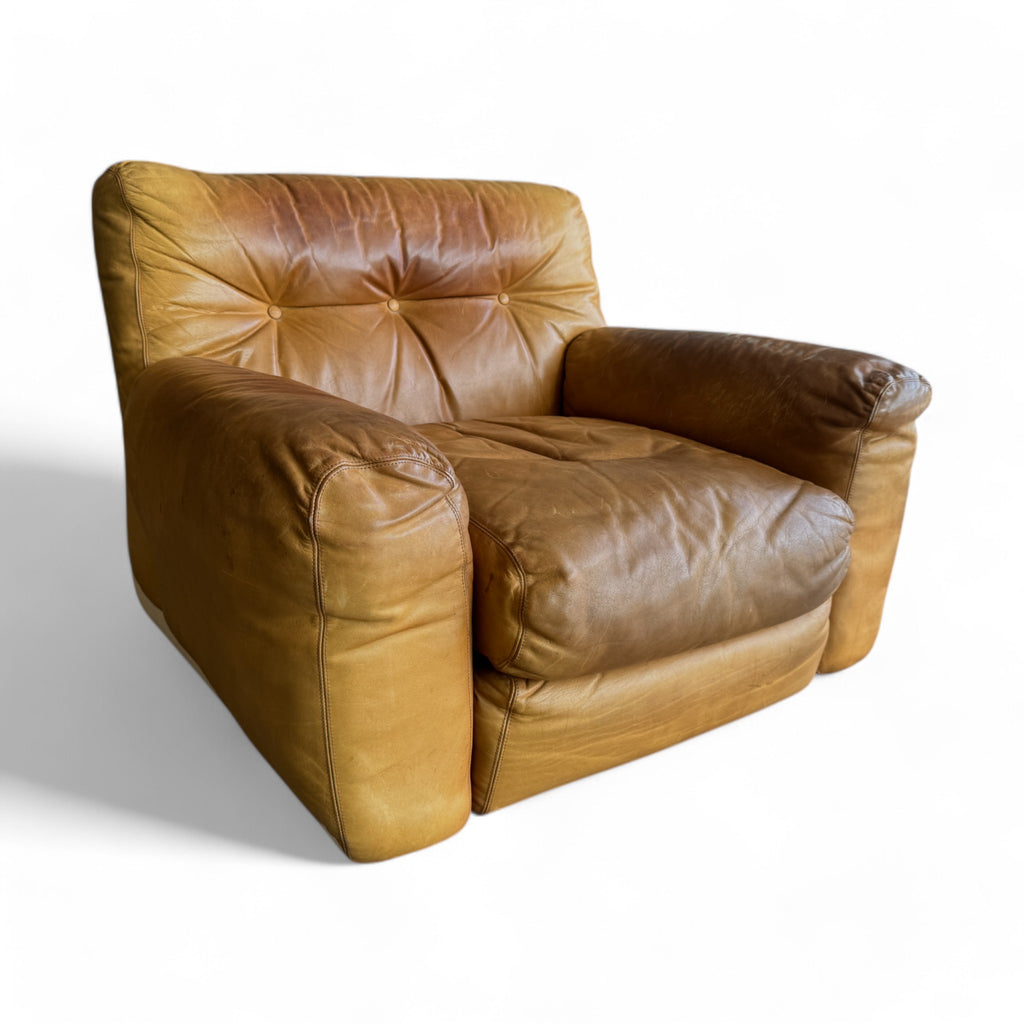 The set has a soft, aged leather in a warm tan shade that shows natural wear, giving it character. The seating is plump and low to the ground, with deep, buttoned tufting on the backrests and seats, creating a cozy, cushioned appearance. The sofa is modular, broken into three sections that align in a straight row, while the armchair has a similar, inviting design with rounded edges. The overall look feels both vintage and comfortably worn, like a well-loved, inviting piece of furniture.