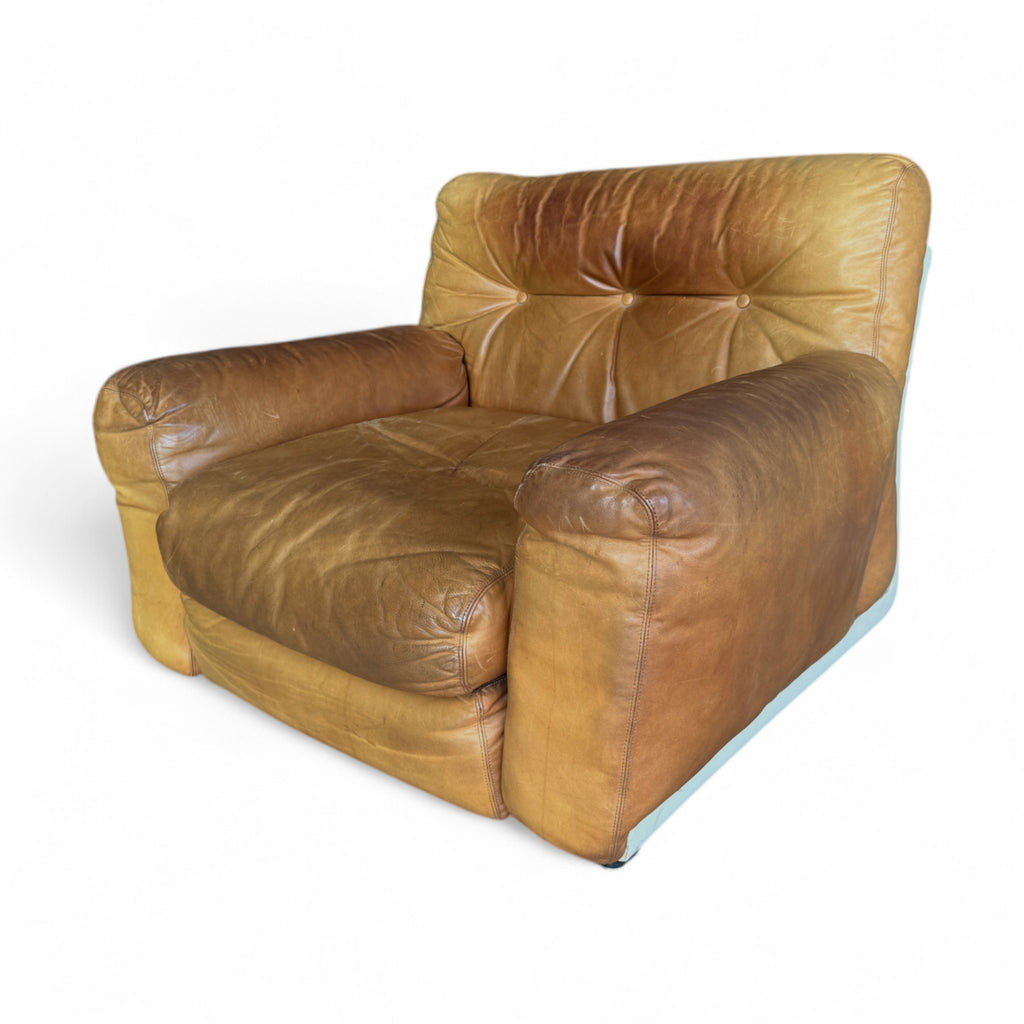 The set has a soft, aged leather in a warm tan shade that shows natural wear, giving it character. The seating is plump and low to the ground, with deep, buttoned tufting on the backrests and seats, creating a cozy, cushioned appearance. The sofa is modular, broken into three sections that align in a straight row, while the armchair has a similar, inviting design with rounded edges. The overall look feels both vintage and comfortably worn, like a well-loved, inviting piece of furniture.