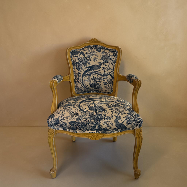deKor vintage armchair with a light wood frame and blue and white floral toile upholstery on a checkered floor