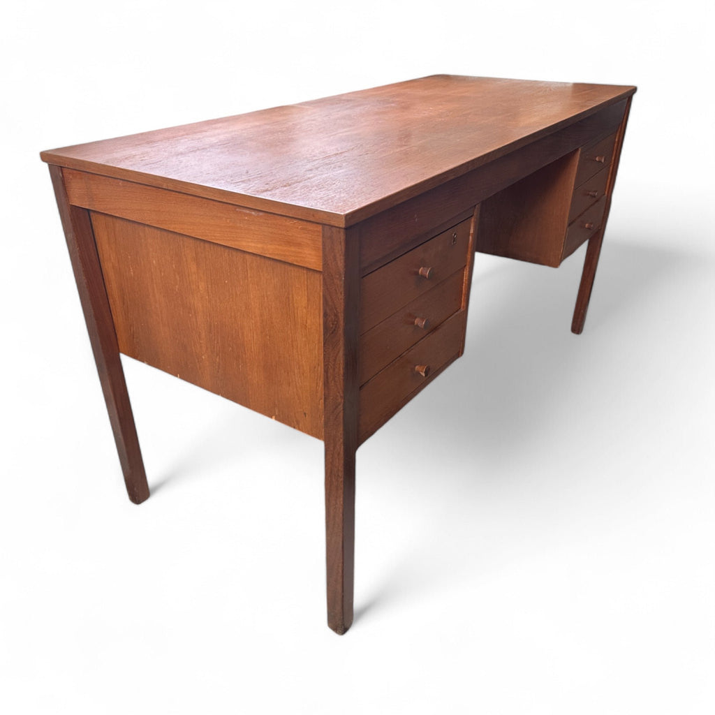 This vintage mid-century desk has a simple, rectangular design with a warm wood finish. It features two sets of drawers on each side, each with three drawers and small wooden pulls. 