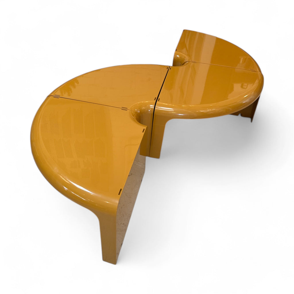 
This table has a smooth, rounded shape with a glossy, almost glass-like surface that feels seamless to the touch. Its design is made up of separate pieces that fit together, creating curved edges and a slightly recessed center. The legs are sturdy and blend into the overall shape, giving it a cohesive, modern feel.