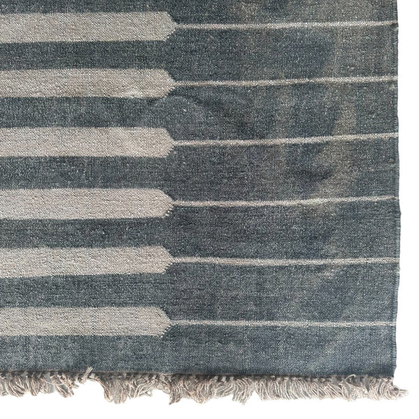 Detail of bottom corner of vintage natural fiber rug with charcoal stripes and fringe