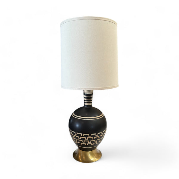 Vintage Black Ceramic Art Deco Table Lamp with white geometric lines etched around the circular base. A brass base props the lamp up and there is a white lampshade. 