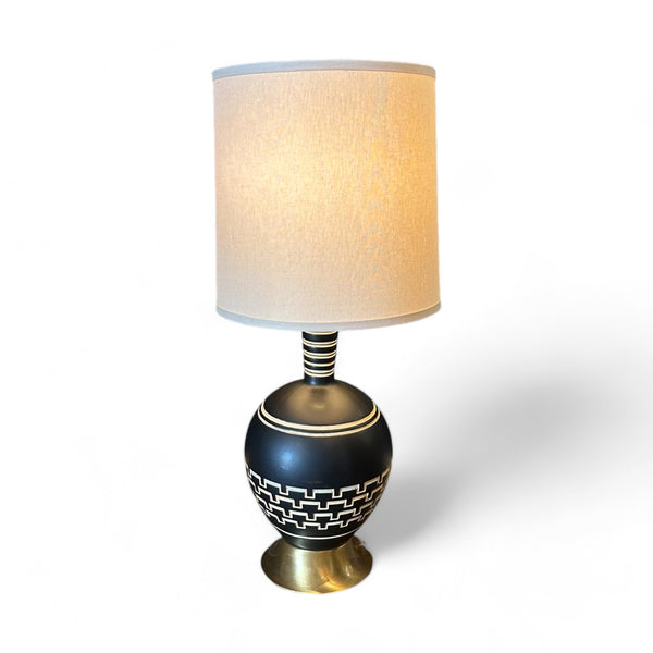 Vintage Black Ceramic Art Deco Table Lamp with white geometric lines etched around the circular base. A brass base props the lamp up and there is a white lampshade. 