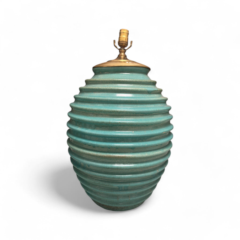 These lamps are shaped like large, rounded ovals with a ribbed texture running horizontally around the entire body. They have a soft green color with brass hardware at the top where the lightbulb fits in. The lamps feel slightly textured due to the ribbing, and the base is wide and sturdy.