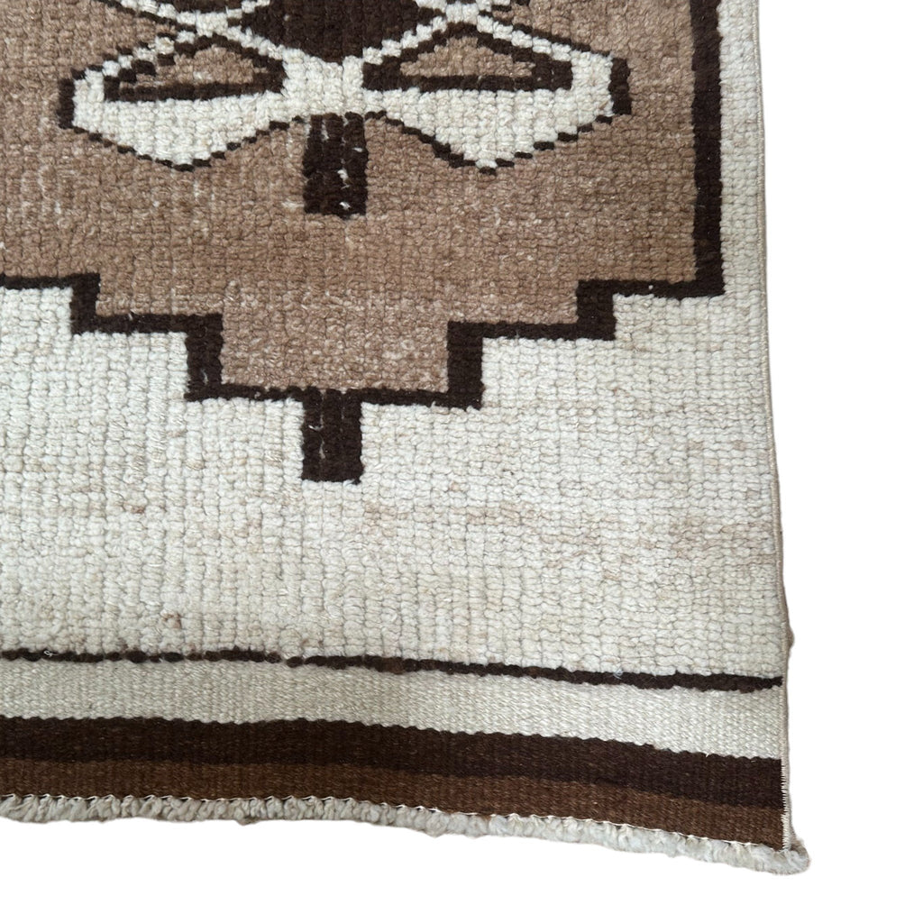 This is a long, narrow rug with a soft, woolen texture. The rug is divided into several sections, each featuring raised, symmetrical patterns with shapes like diamonds and crosses. The colors are muted and natural, blending soft brown and beige, giving it a warm, rustic feel.