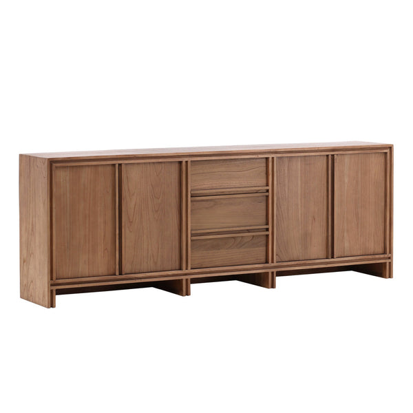 This credenza is a long, rectangular piece of furniture made of smooth, solid wood with a natural finish. The front of the credenza has a minimalist design, featuring four large cabinet doors on either side and three smaller drawers in the center. The overall look is clean and modern, with subtle, precise lines that give it a sense of refined simplicity. The wood has a slightly warm tone, adding a touch of natural beauty to the piece.