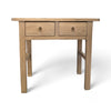 This table is rectangular, made from sturdy, rough-textured wood with a natural finish. It has four thick legs, standing firmly on the ground, and is about waist-high. The front has two drawers, each with a small brass ring handle you can pull, and the overall feel is rustic, as if the wood has been well-worn but carefully crafted. The edges are smooth but the surface has a slight grain that feels natural and earthy.