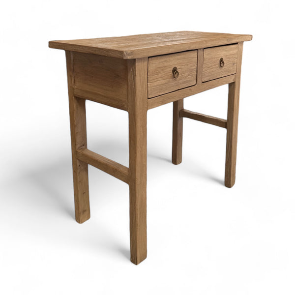 This table is rectangular, made from sturdy, rough-textured wood with a natural finish. It has four thick legs, standing firmly on the ground, and is about waist-high. The front has two drawers, each with a small brass ring handle you can pull, and the overall feel is rustic, as if the wood has been well-worn but carefully crafted. The edges are smooth but the surface has a slight grain that feels natural and earthy.