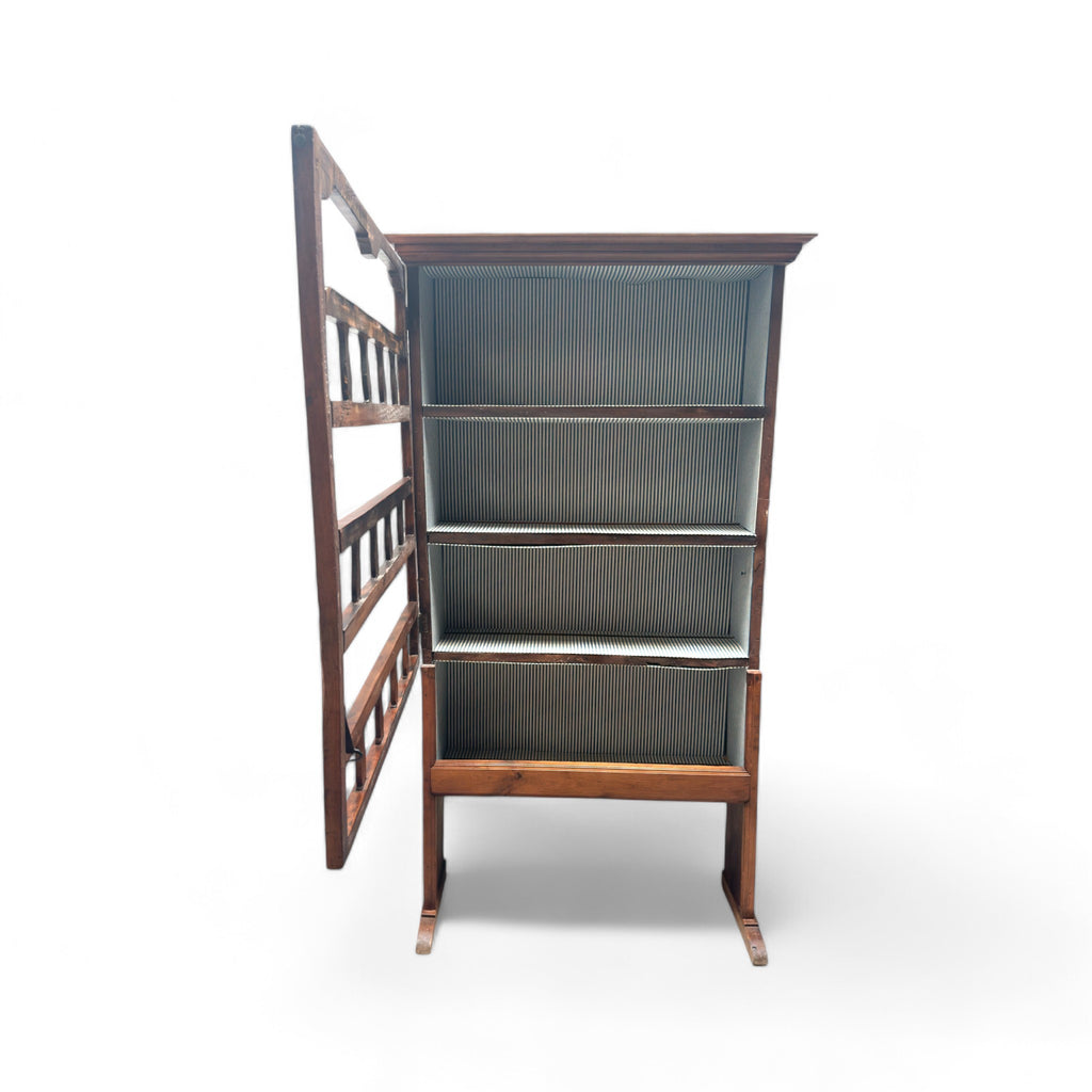 This 19th-century Provincial kitchen hutch, or "plate rack," is a tall, narrow wooden cabinet, standing freely on the floor. It has five shelves, each lined with a fabric featuring thin vertical stripes. The shelves are open at the front, with wooden slats that act like barriers to hold plates in place. The wood has a warm, aged texture, with a smooth yet slightly worn feel from years of use. The left side of the hutch has a hinge, allowing the front to swing open, secured with a simple iron latch. 