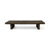 This rectangular coffee table is made of dark, textured wood. The tabletop is thick and flat, supported by two solid, block-like legs on either side. The wood appears rough and natural that add to its rustic, handcrafted appearance.