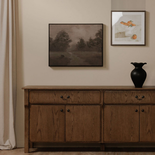 deKor Alder framed painting featuring a moody woodland landscape in deep purple tones hanging above a wooden sideboard.