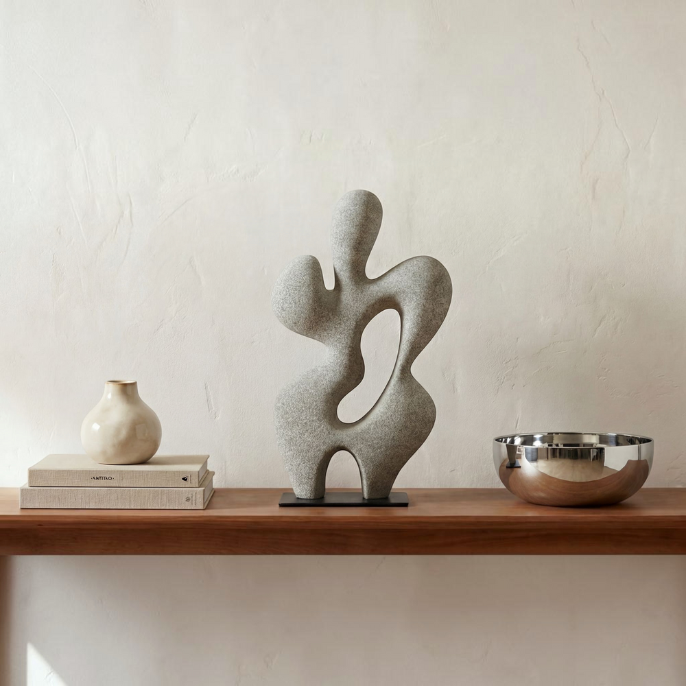 deKor charcoal grey freeform modernist sculpture made of Ecomix on a thin black metal base against a tan background.