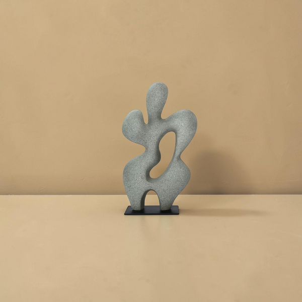 deKor charcoal grey freeform modernist sculpture made of Ecomix on a thin black metal base against a tan background.