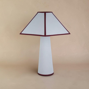 deKor cotton-wrapped table lamp with a white tapered base and a geometric shade featuring dark red trim.