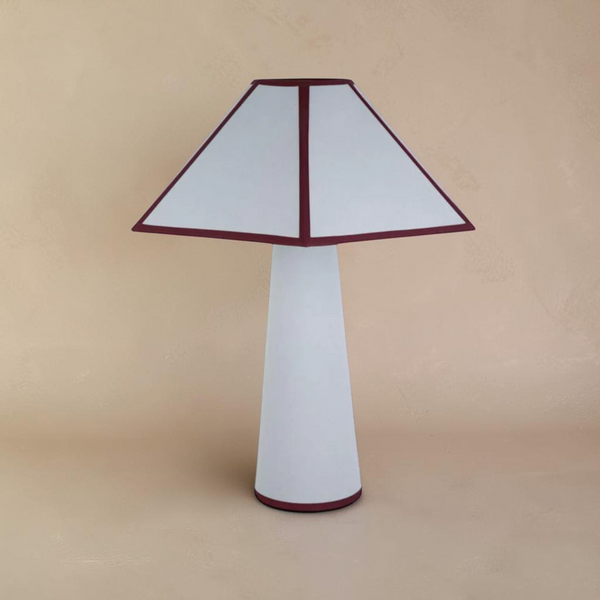 deKor cotton-wrapped table lamp with a white tapered base and a geometric shade featuring dark red trim.