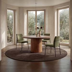 deKor set of two green upholstered dining chairs with curved iron frames and cushioned seats in a bright dining room.