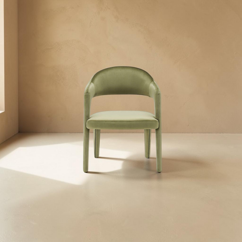 deKor green velvet dining chair with a curved barrel back and armrests in a minimalist room setting