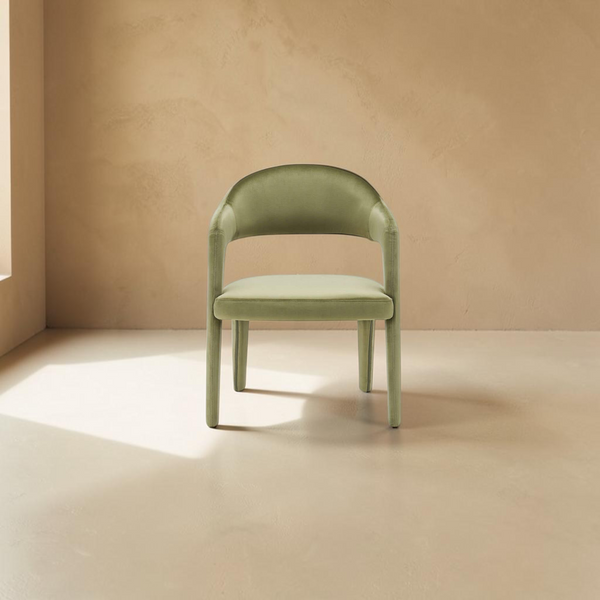 deKor green velvet dining chair with a curved barrel back and armrests in a minimalist room setting