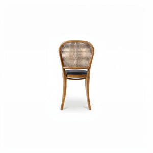 deKor rattan dining chair with a natural wood frame, woven cane backrest, and a dark polyurethane seat.