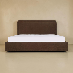 deKor Simon storage bed in dark brown fabric with a rounded headboard and piped detailing, front view.