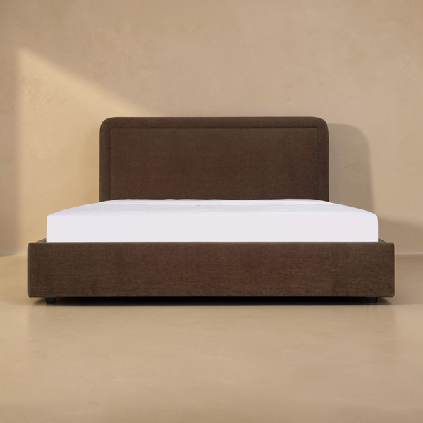 deKor Simon storage bed in brown fabric with a rounded headboard and piped detailing, front view.