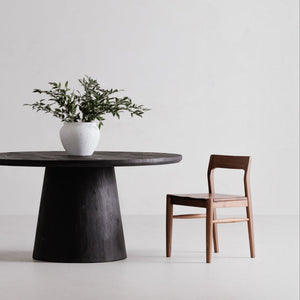 deKor solid walnut dining chair with a curved open-back design and mid-century silhouette next to a round table.