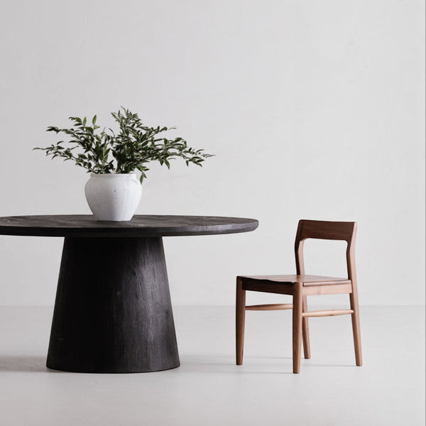 deKor solid walnut dining chair with a curved open-back design and mid-century silhouette next to a round table.