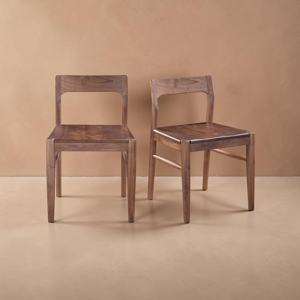 deKor set of two solid walnut dining chairs featuring a mid-century modern curved open-back design in walnut brown.