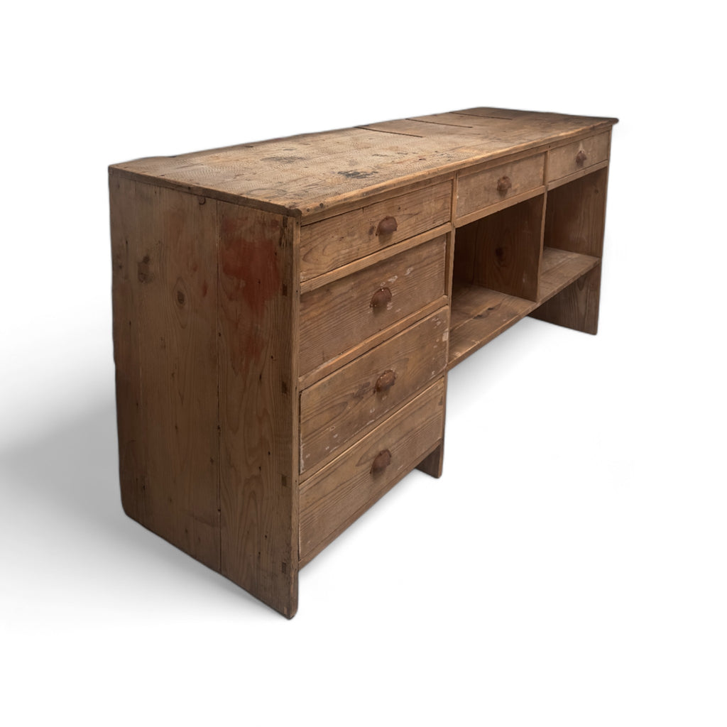 large, rectangular wooden sideboard with a rustic and aged appearance. It has six drawers on the left side, arranged in two columns of three, each with a simple wooden knob. The middle section features two additional drawers at the top, with open storage compartments below them. The wood has a natural, weathered look with some visible wear and imperfections, adding to its vintage charm.