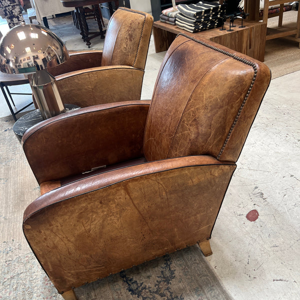 Brown leather club chairs on a patterned rug and books in the background