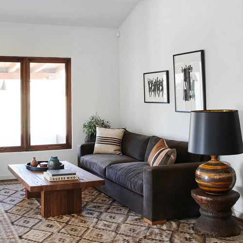 Sofa in livingroom with vintage midcentury ceramic lamp, framed art on wall and wood plank coffee table.