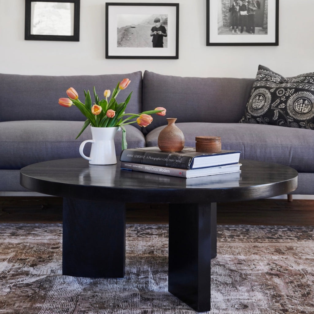Round mcm coffee table made from sustainable alder wood in black finish showing styling inspiration with art books and floral arrangement