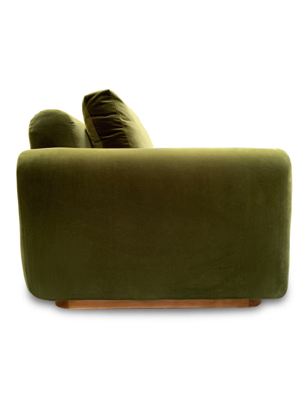 Side view of custom made green velvet sofa with natural wood base and sloped back